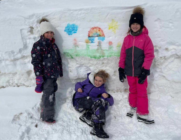 Trois enfants devant un banc de neige avec des dessins