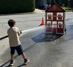 Enfant utilisant une lance à eau vers la maquette d'une maison en flamme...